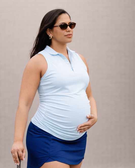 Pregnant woman wearing a light blue sleeveless top and blue skirt against a neutral background